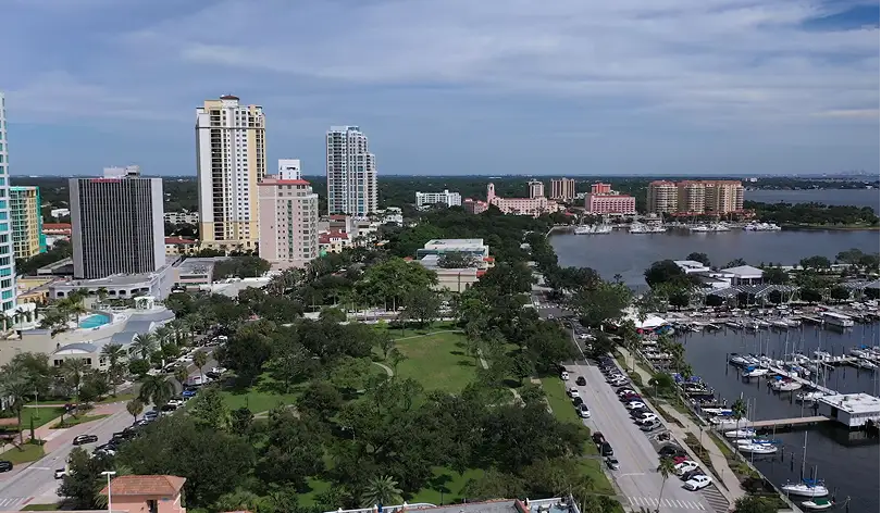 Aerial view of a waterfront city with high-rise buildings, roads, and a marina under cloudy sky