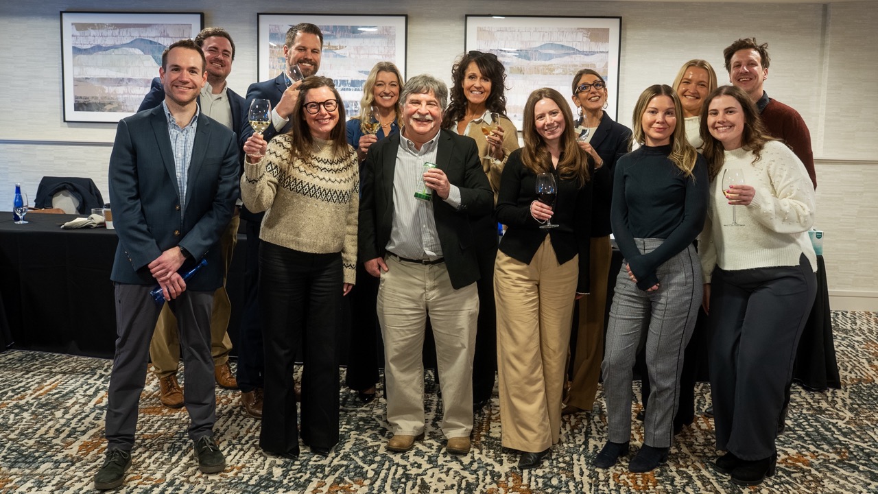Group of professionals in suits and dresses toasting with wine glasses at an indoor PR event.