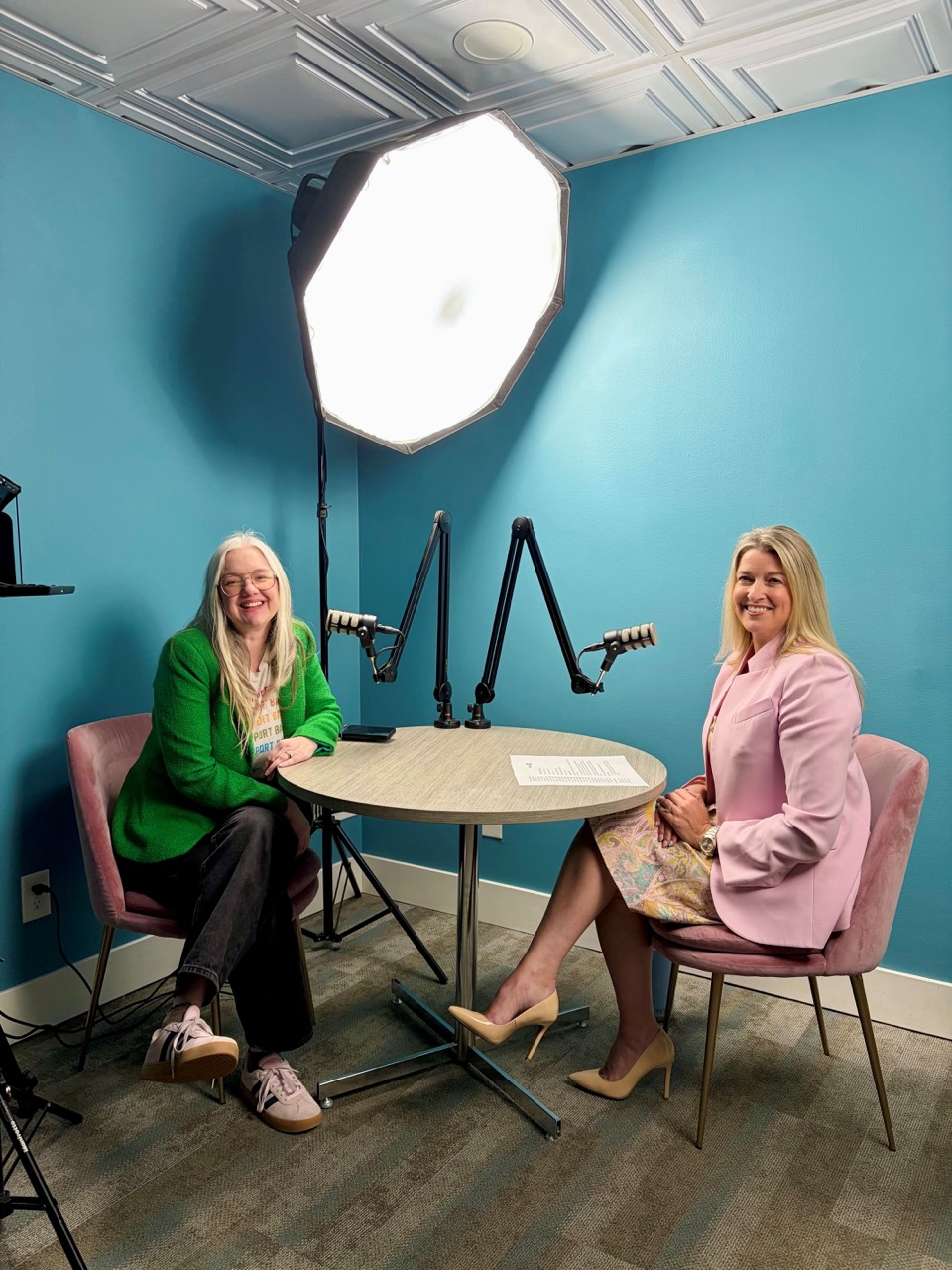 Two women seated in a studio, smiling under bright ring light for a PR firm interview