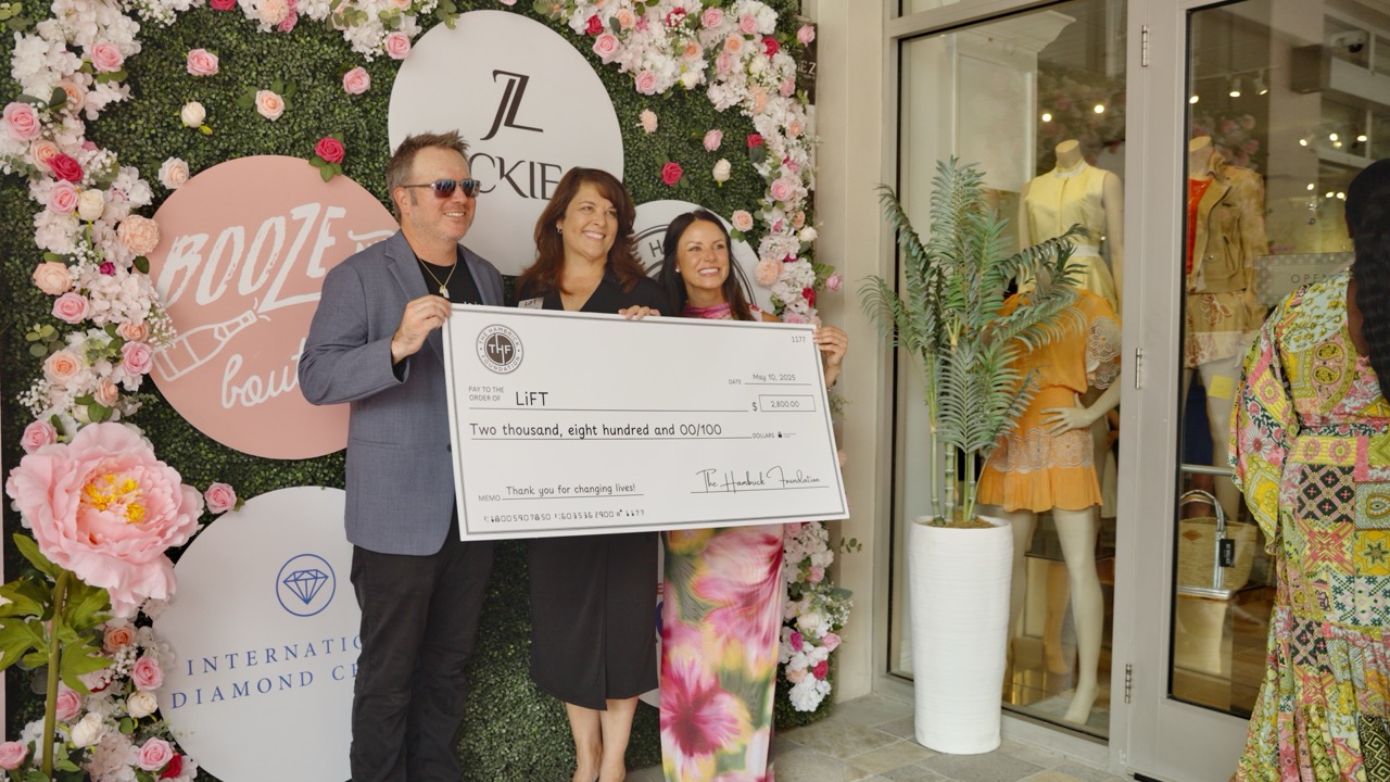 Group holding a large check, “PAY TO THE ORDER OF LIFT,” amid International Diamond Collection flowers